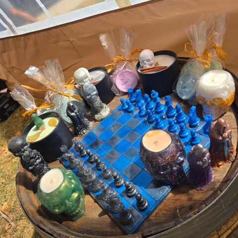 A chess set at our stall: a blue and black board with dark pieces on a barrel top, among candles and little skulls.