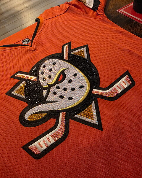 The front of an orange hockey jersey, its crest covered in rhinestones.