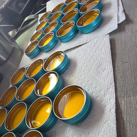Rows of open teal tins filled with freshly poured golden leather balm.