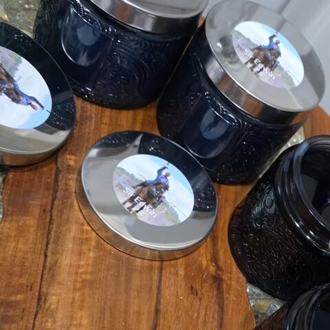 Dark carved-glass candle jars with silver lids, each lid showing a jouster on horseback.